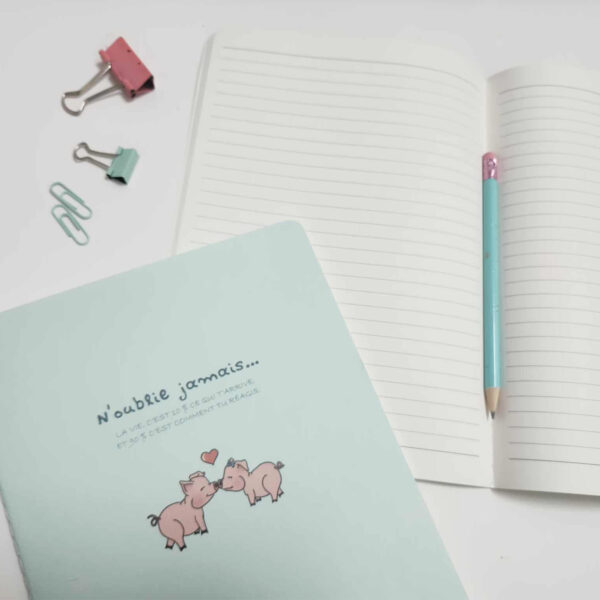 Carnet de notes cousu bleu avec illustration de cochons mignons et citation motivante, ouvert sur pages lignées avec accessoires