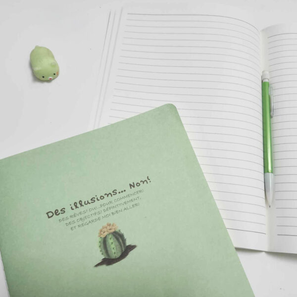Carnet de notes cousu vert avec illustration de cactus et citation motivante, ouvert sur pages lignées avec accessoires verts