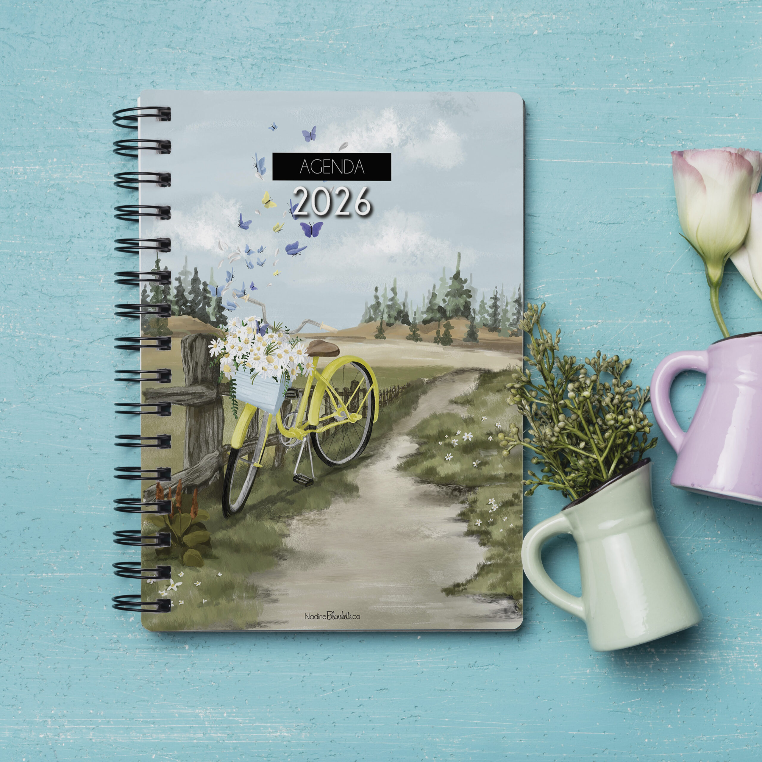 Agenda 2026 Vents de changement posé sur une surface turquoise avec une tasse et des fleurs